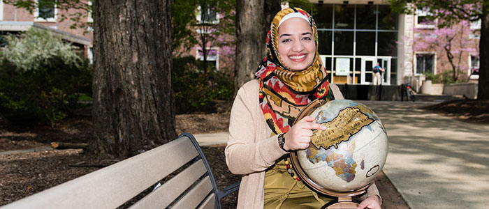 Sarah Khan sitting, pointing to Turkey on a globe