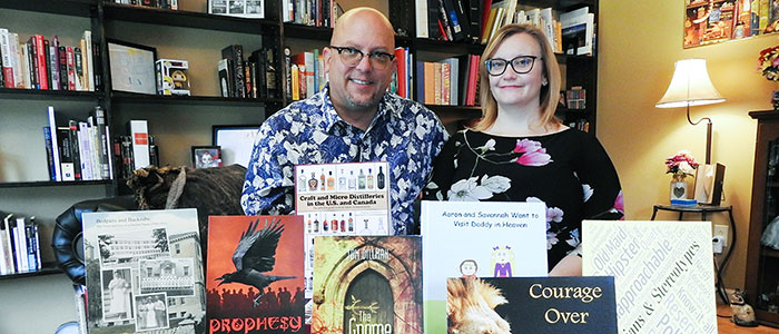 Christina Steffy poses with her husband David J. Reimer Sr. pose in front of books at their publishing company, Crave.